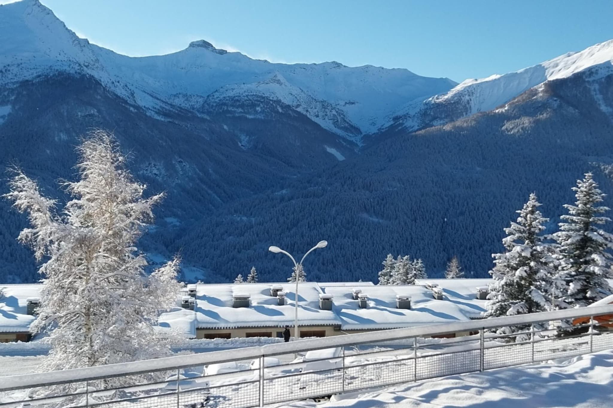 Eine verschneite Berglandschaft mit einem Gebäude mit geneigtem Dach und einem eingezäunten Bereich im Vordergrund.