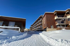A snow-covered street with multi-story buildings, including a hotel with balconies and a wooden facade. - Alpine Ski Apartment in Tignes for 4 (Orcières)