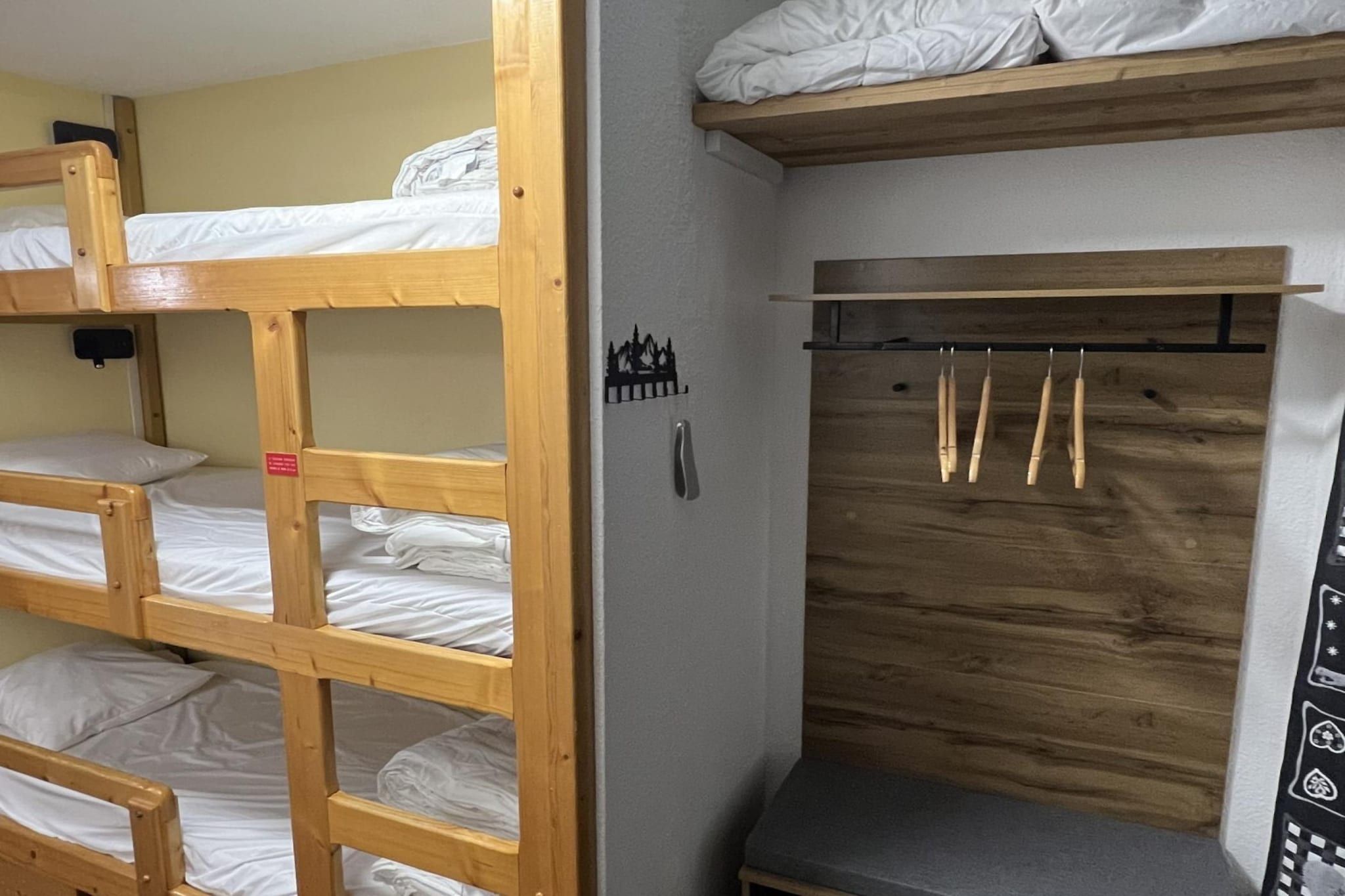 Habitación con literas, un armario de madera y un pequeño banco.