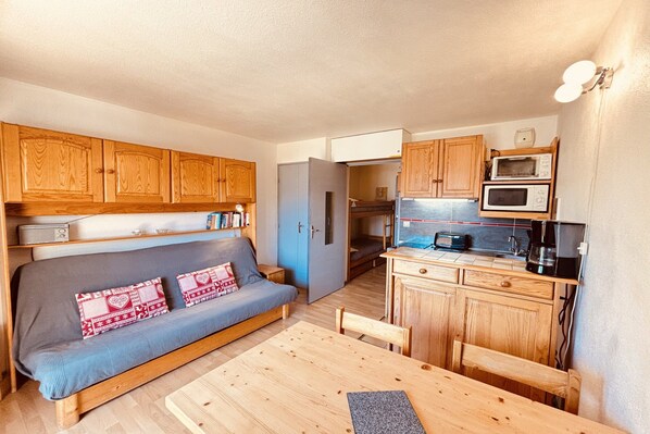 A compact living space with a sofa, a dining table, wooden cabinets, and a kitchenette. - Cozy Mountain-View Apartment in Les Deux Alpes for 4 (Les Deux Alpes)
