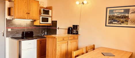 Cocina compacta con armarios de madera, microondas, cafetera y una pequeña mesa de comedor con sillas.