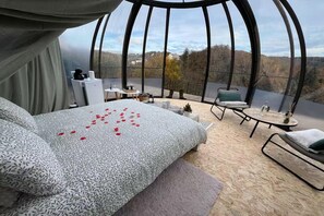 Een slaapkamer met een groot bed, een bureau, een stoel en uitzicht op het groen via een glazen dak.