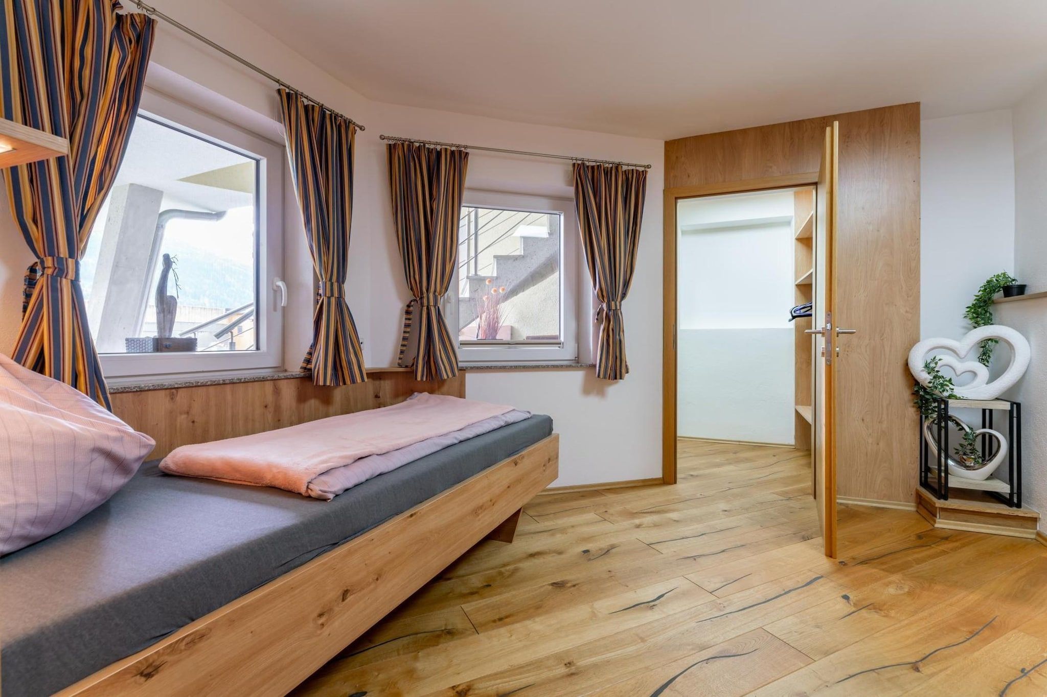 Una habitación con una cama, piso de madera y una puerta que da a otra estancia.
