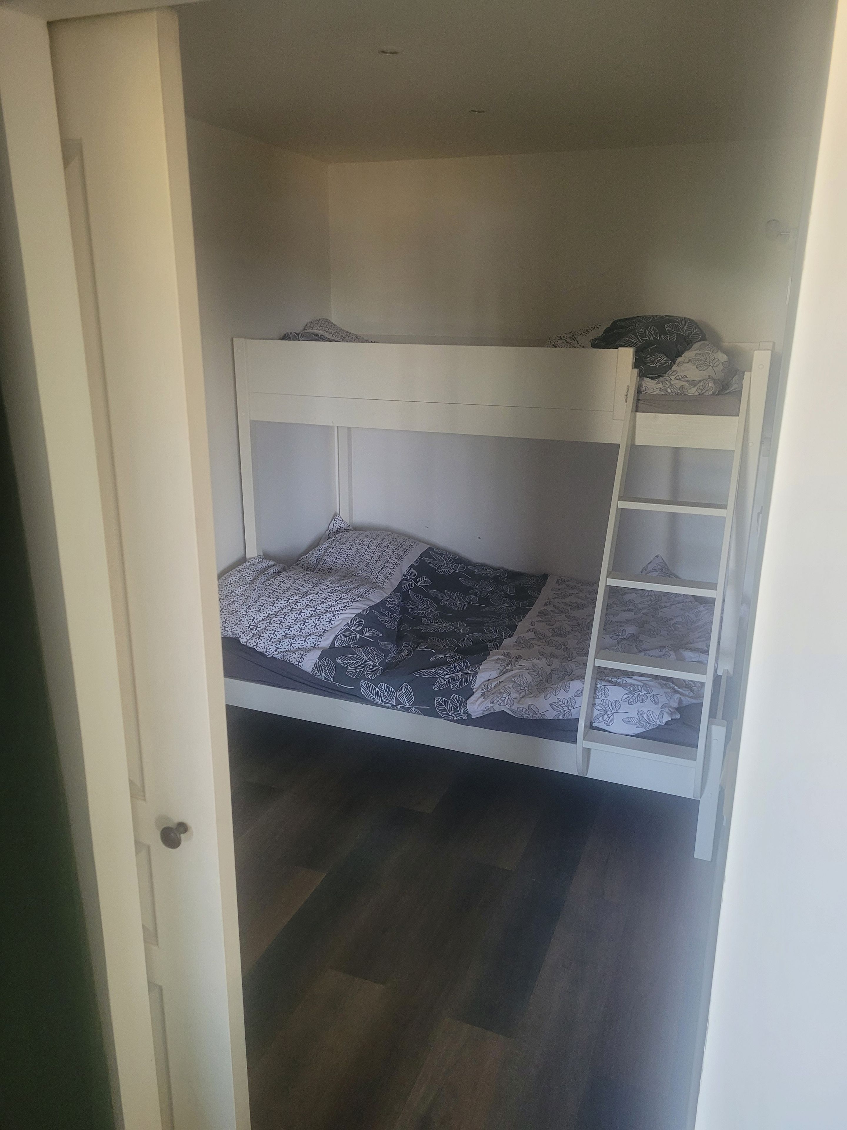 A bunk bed with a ladder, a door, and a patterned bedspread.