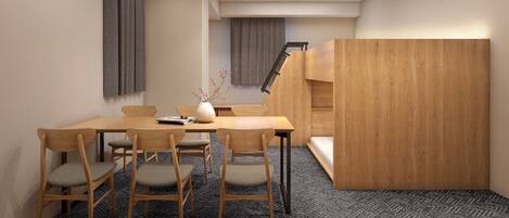 A modern interior with a wooden dining table, four chairs, a vase with branches, and a staircase leading to an upper level.