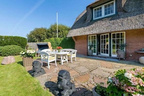 A house with a thatched roof, a patio with stone flooring, and a garden with a statue. - Holiday home Dünensand (Kampen)