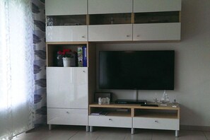 A modern entertainment unit with a flat-screen TV, built-in shelving, and a small wooden shelf with decorative items. - Holiday home with 2 bedrooms (Wangerland Hooksiel)