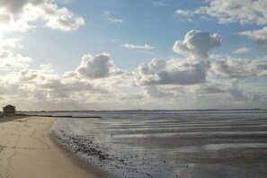 Une plage avec un rivage sablonneux, un petit bâtiment et une mer calme sous un ciel nuageux.