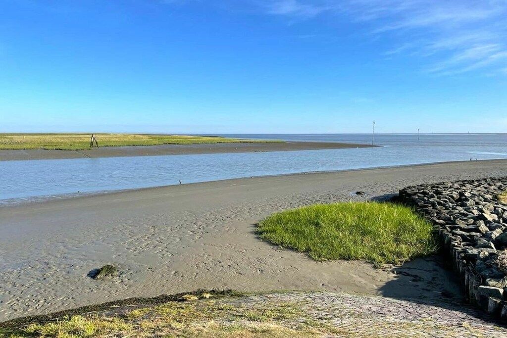 A coastal landscape with a sandy beach, a grassy area, and a stone wall.
