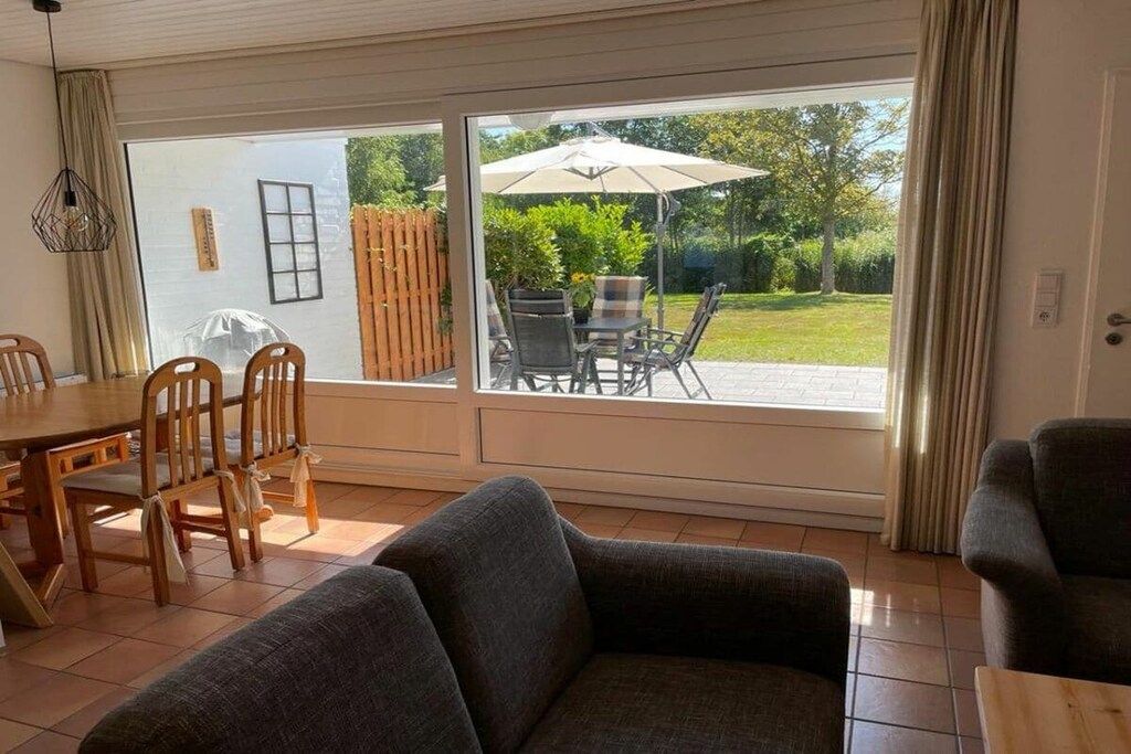 A living room with a sofa, dining table, chairs, and a sliding glass door leading to an outdoor patio with a table and chairs.