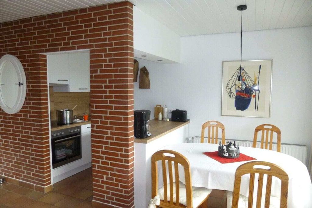 Une cuisine compacte avec un mur en briques, des meubles blancs et un coin repas comprenant une table et des chaises.