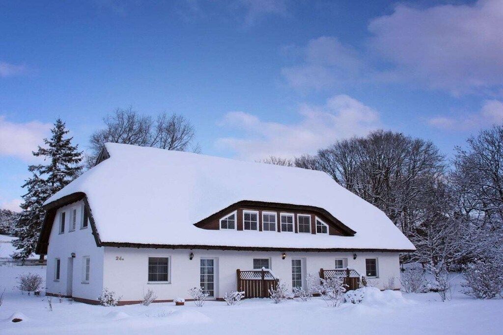 A white house with a sloped roof, surrounded by snow-covered trees and a clear sky.