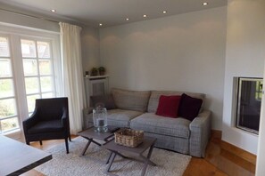 Una sala de estar moderna con un sofá gris, un sillón negro, una mesa de centro y un ventanal con cortinas.