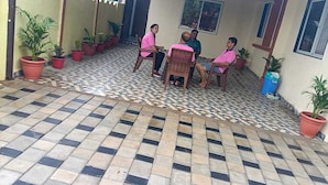 A covered outdoor seating area with potted plants and a tiled floor.