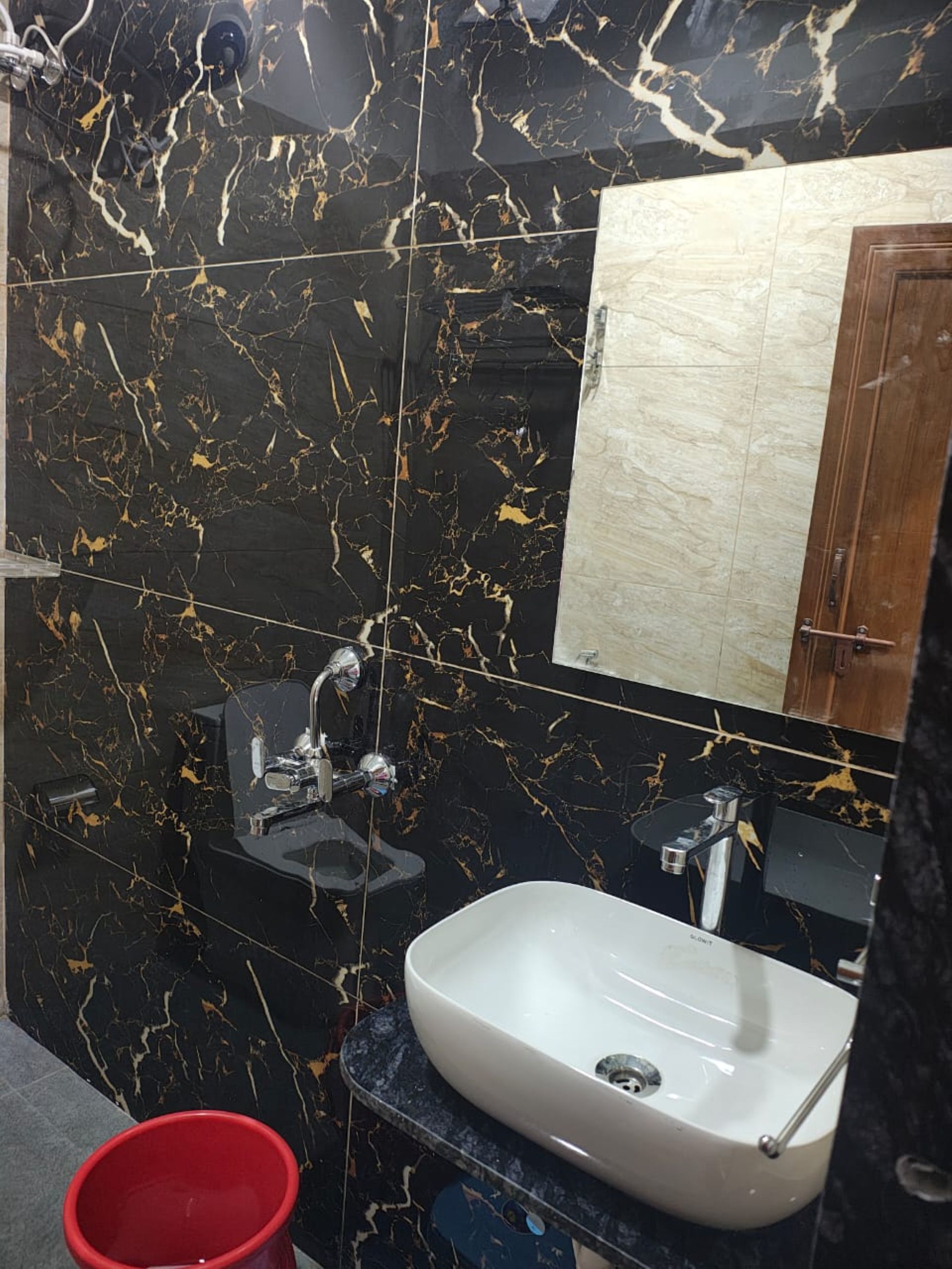 Une salle de bain avec un mur en marbre noir, un lavabo blanc et un meuble en bois.
