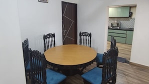 Un coin repas avec une table ronde et quatre chaises, un ventilateur de plafond et une cuisine en arrière-plan.