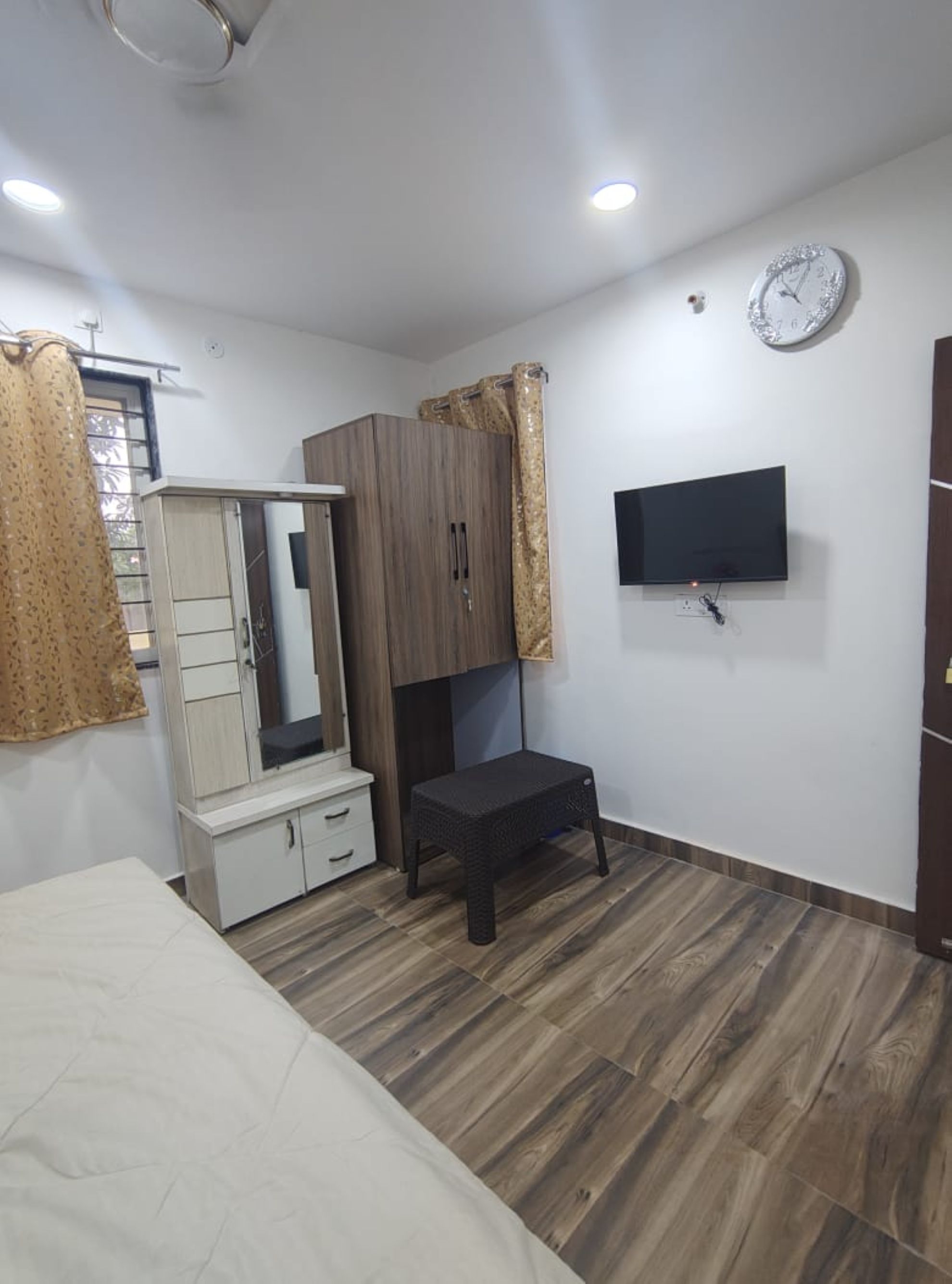 Un dormitorio con cama, armario, televisor y un reloj en la pared.