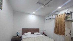 Une chambre à coucher comprenant un lit, des tables de chevet, un appareil de climatisation, une armoire et un ventilateur de plafond.