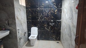 Une salle de bain avec des toilettes, un lavabo et une douche. Il y a des seaux rouges et un seau rouge sur le sol.