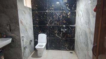 Un baño con inodoro, lavamanos y ducha. Hay cubetas rojas y una cubeta roja en el suelo.