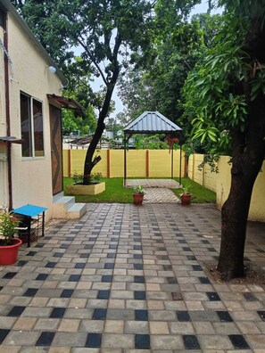 A courtyard with a paved walkway, a small table, potted plants, and a gazebo.