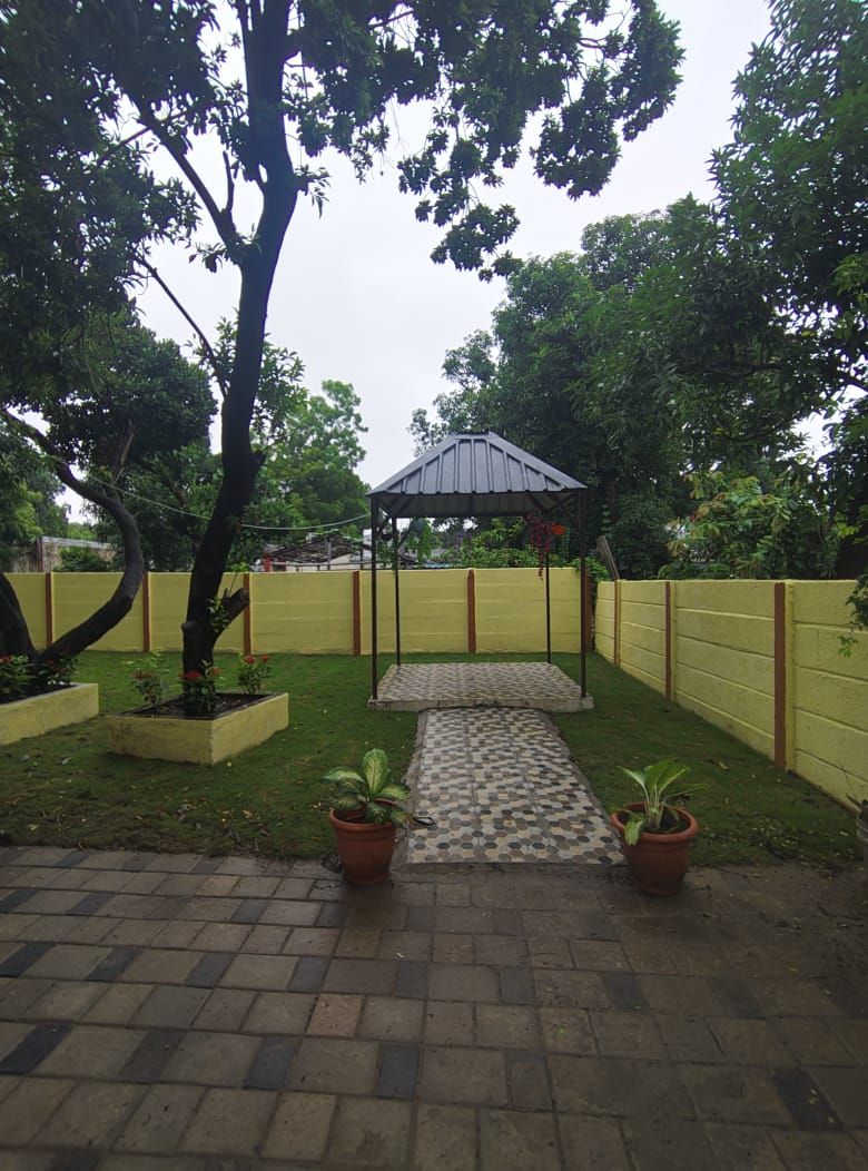 A covered outdoor area with a paved walkway, surrounded by a yellow fence and greenery.