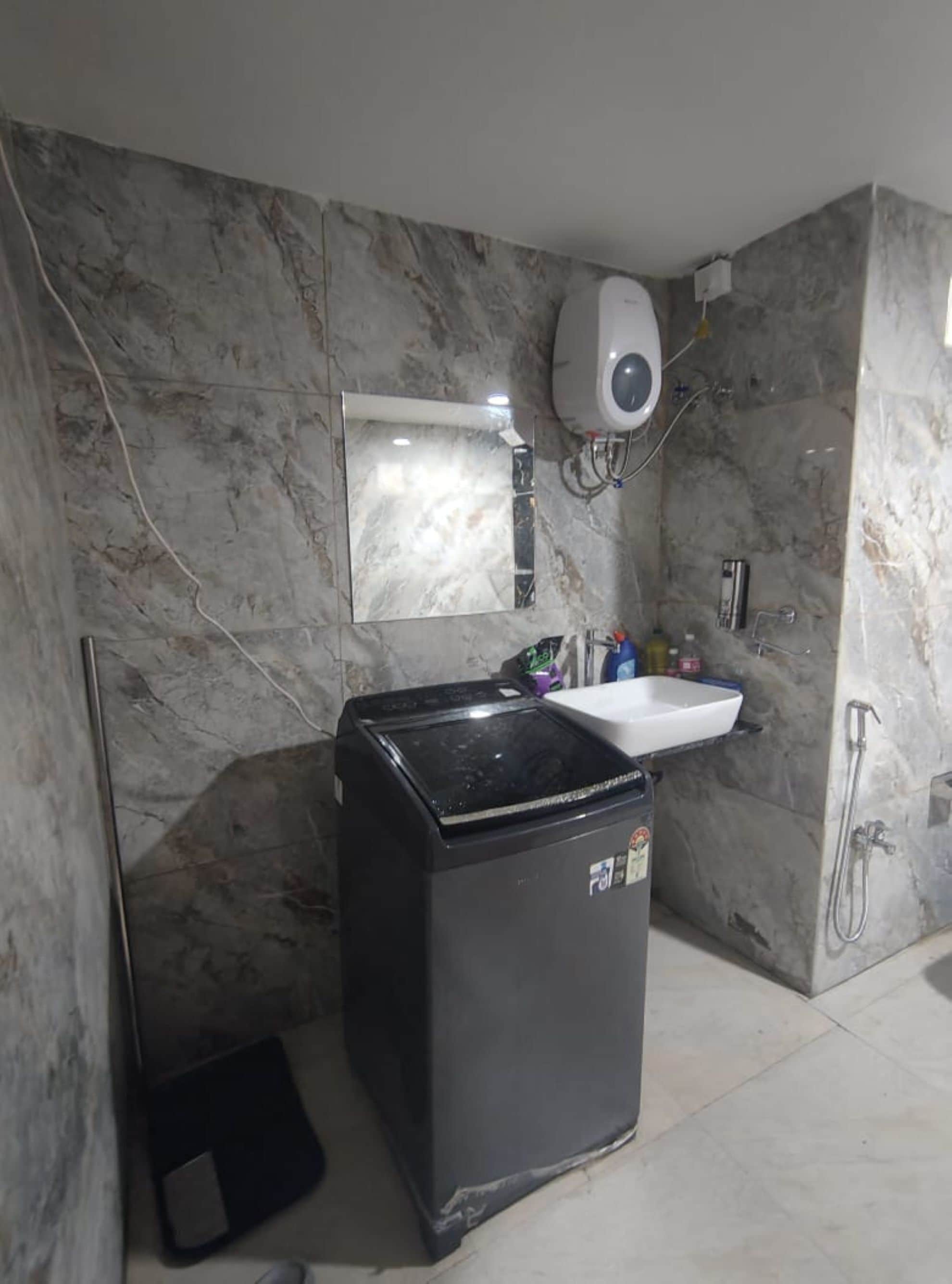 A compact bathroom with a marble wall, a white sink, a black trash bin, and a handheld showerhead.