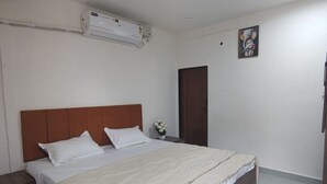 A hotel room with a bed, a nightstand, a wall-mounted air conditioner, a door, and a ceiling fan.