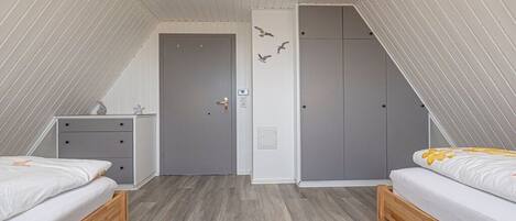 Een slaapkamer met twee bedden, een dressoir, een kledingkast en een deur met lichtschakelaar.