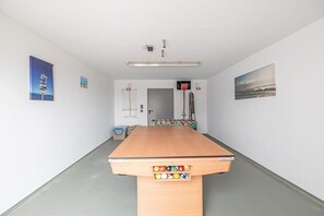 A billiards table with balls, a foosball table, and wall-mounted sports equipment in a room with white walls and a gray floor. - Holiday home with 2 bedrooms (Nordstrand)