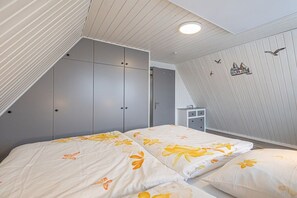 Ein Schlafzimmer mit schrägverdeckter Decke, einem Bett mit floralem Bettbezug, einem Kleiderschrank und einem kleinen Nachttisch.