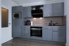 A compact kitchen with grey cabinets, a built-in microwave, a stove, and a coffee maker. - Holiday apartment with 2 bedrooms (Carolinensiel)