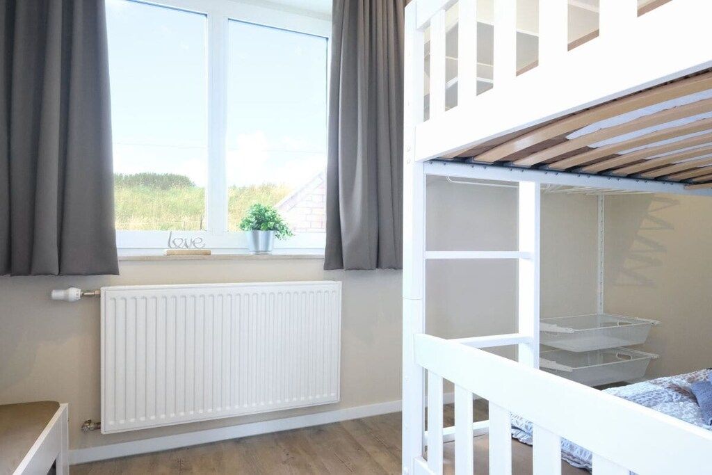 Una habitación con literas, un radiador, una ventana con cortinas y vistas al exterior.