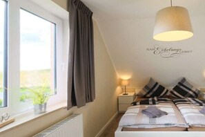 Een slaapkamer met een bed, nachtkastje, lamp, raam met gordijnen en een wandbord.