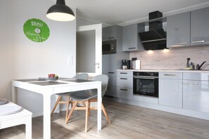 A modern kitchen with grey cabinets, a black range hood, and a white dining area with a table and chairs. - Holiday apartment with 2 bedrooms (Carolinensiel)