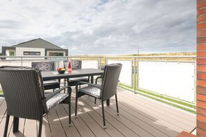 An outdoor deck with a table and chairs, a view of a building, and a grassy area in the background. - Holiday apartment with 2 bedrooms (Carolinensiel)