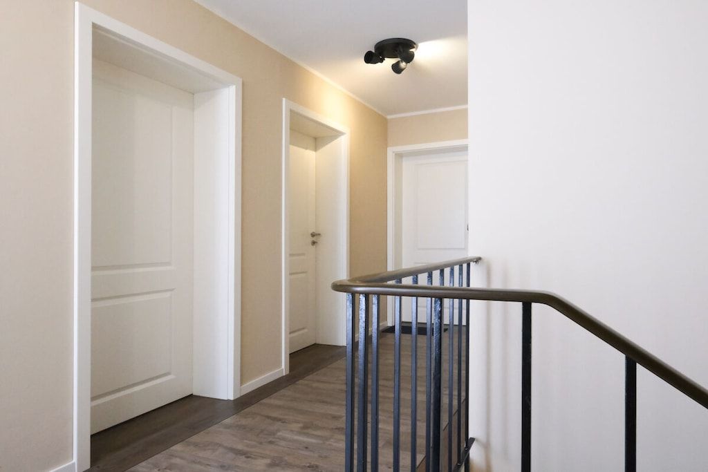 A hallway with a wooden floor, white doors, and a metal railing.