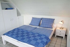 Quarto com cama, duas almofadas, mesa de cabeceira com abajur e guarda-roupa.