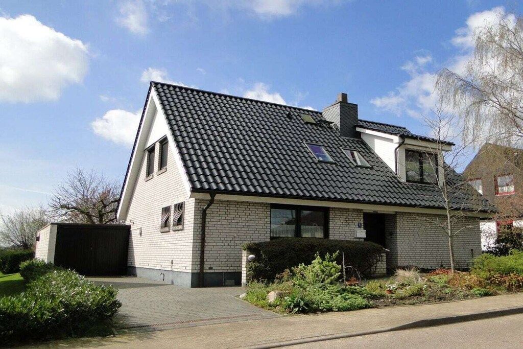 Een huis met twee verdiepingen, een pannendak, een garage en een verzorgde tuin.