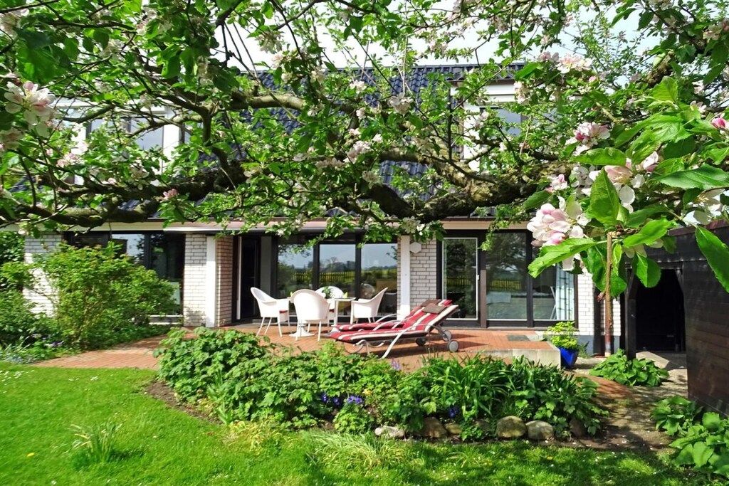 A modern house with a patio, white chairs, and a red lounge chair.