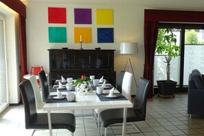 Uma sala de jantar com uma mesa posta para seis pessoas, cadeiras, um armário preto e uma planta em vaso.