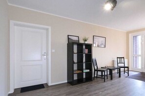 Una habitación con una puerta blanca, una estantería negra, dos sillas, una mesita y un radiador.