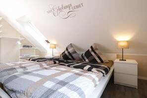 Een slaapkamer met een bed, twee bedlampen, een nachtkastje, een wandplank en een plafondlamp.