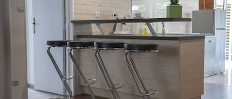 Cozinha moderna com ilha central, banquetas de aço inoxidável e um vaso de planta no balcão.