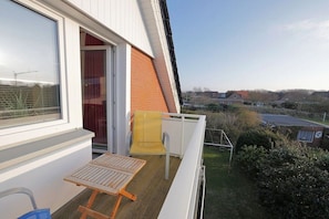 A balcony with a table and chairs, a window, and a view of the surrounding area. - Seestern No. 4 Apartment House Seestern (Norderney)