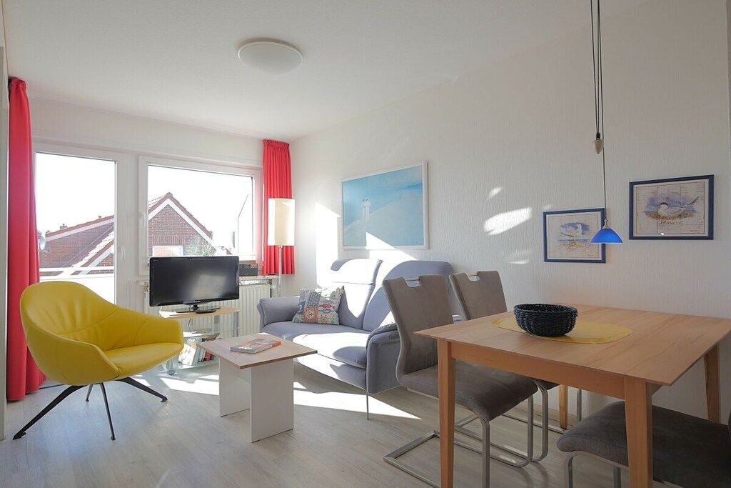 Un salon moderne avec un canapé, un fauteuil jaune, un téléviseur et une table à manger.