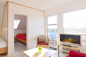 A compact room with a bed, a television, a chair, and a table. - Seestern No. 4 Apartment House Seestern (Norderney)