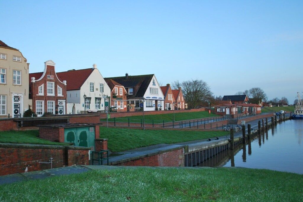 Eine Stadt am Kanal mit historischen Gebäuden, einer grünen Wiese und ruhigem Gewässer.