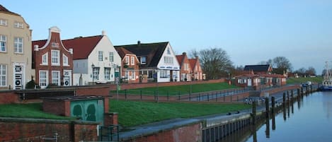 A canal-side town with historic buildings, a green lawn, and a calm waterway.