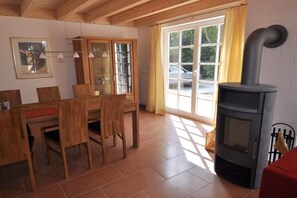 Una habitación acogedora con una mesa y sillas de madera, estufa integrada y un ventanal con cortinas.